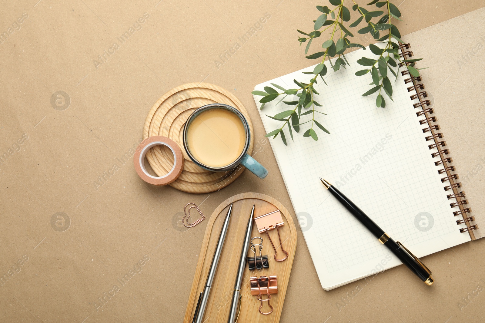 Photo of Binder clips, other stationery, coffee and green branches on beige background, flat lay. Space for text