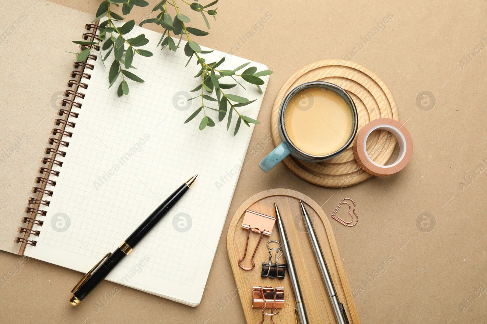 Photo of Binder clips, other stationery, coffee and green branches on beige background, flat lay