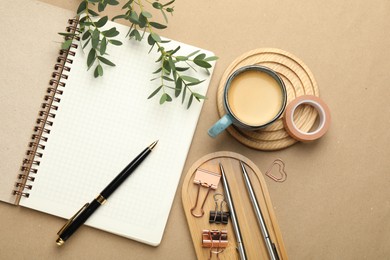 Binder clips, other stationery, coffee and green branches on beige background, flat lay