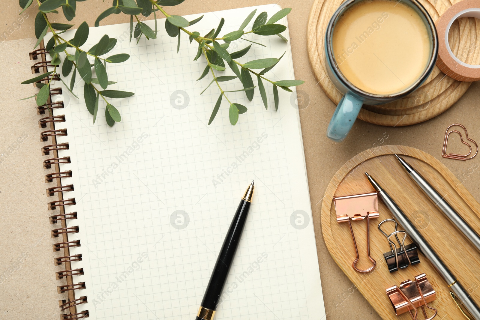 Photo of Binder clips, other stationery, coffee and green branches on beige background, flat lay