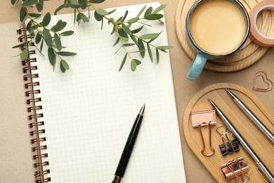 Binder clips, other stationery, coffee and green branches on beige background, flat lay