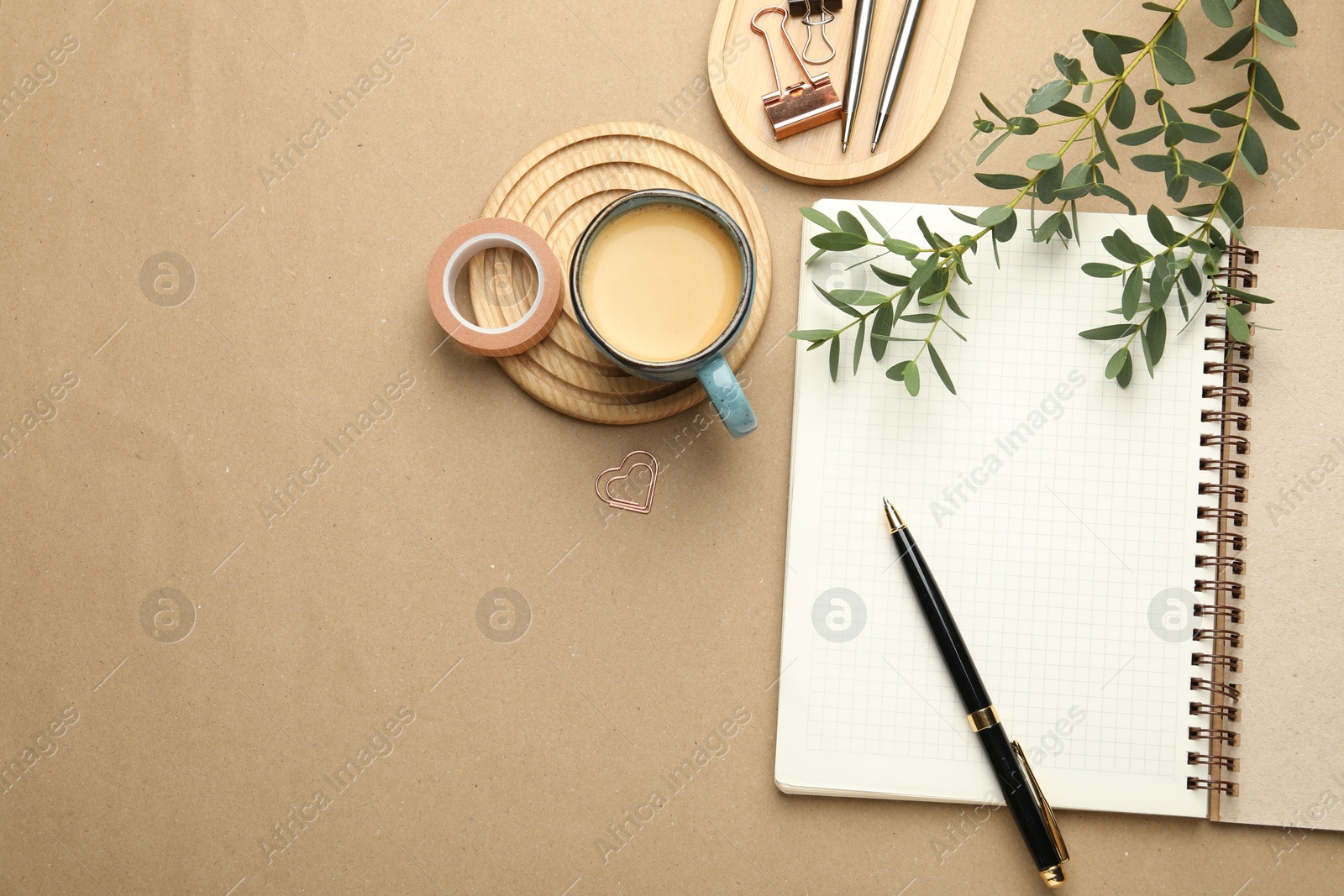 Photo of Binder clips, other stationery, coffee and green branches on beige background, flat lay. Space for text