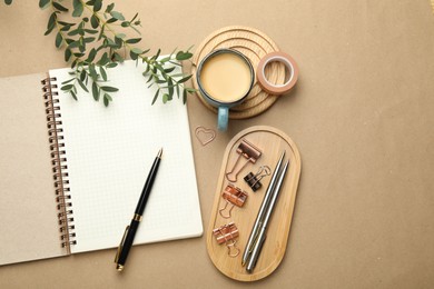 Photo of Binder clips, other stationery, coffee and green branches on beige background, flat lay. Space for text