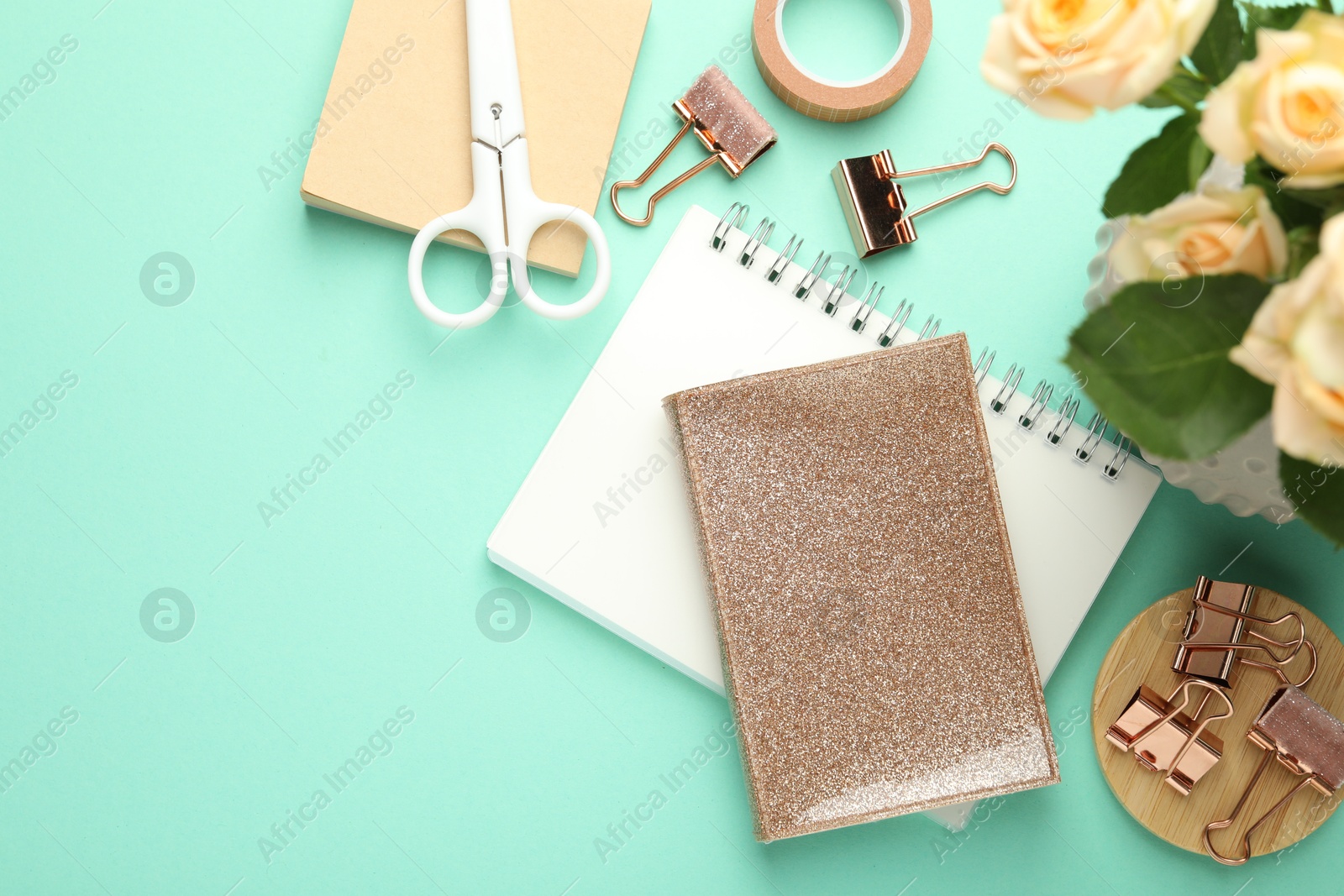 Photo of Binder clips, other stationery and roses on turquoise background, flat lay. Space for text