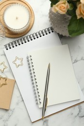 Paper clips, notebooks and decor on white marble table, flat lay