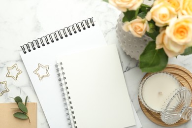 Paper clips, notebooks and decor on white marble table, flat lay