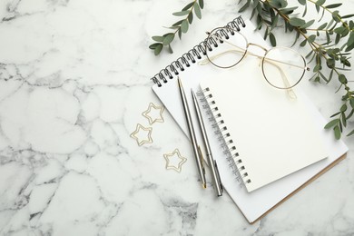 Photo of Paper clips, notebooks, pens, glasses and green branches on white marble table, flat lay. Space for text