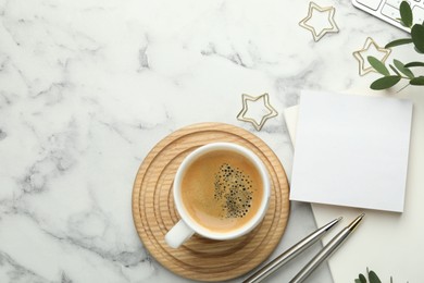 Paper clips, other stationery, coffee and green leaves on white marble table, flat lay. Space for text