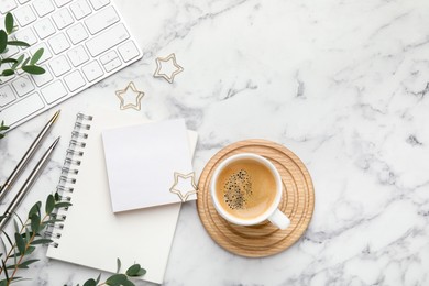 Paper clips, other stationery, coffee, computer keyboard and green branches on white marble table, flat lay. Space for text