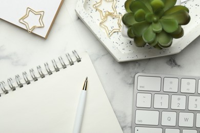 Paper clips, other stationery, decor and computer keyboard on white marble table, flat lay