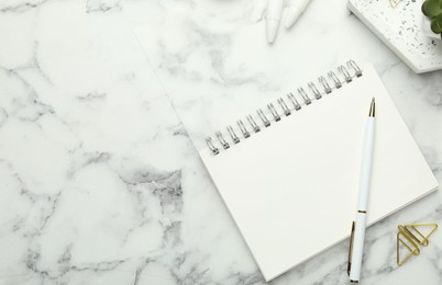 Photo of Paper clips, notebook and pen on white marble table, flat lay. Space for text