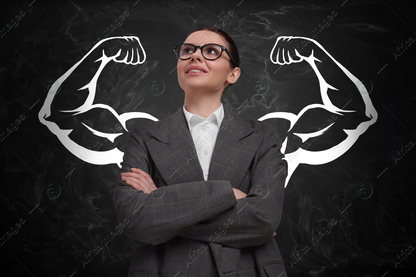 Image of Confident business woman with drawing of strong arms behind her on black chalkboard