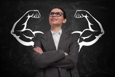 Image of Confident business woman with drawing of strong arms behind her on black chalkboard