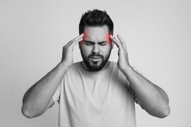 Image of Young man suffering from headache on light background. Black and white effect with red color accent