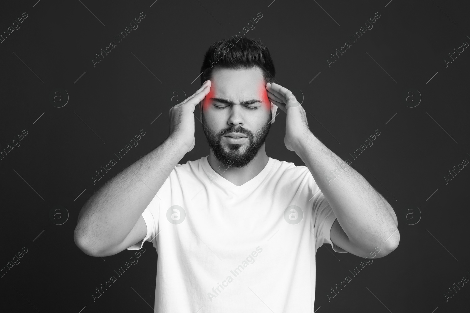 Image of Young man suffering from headache on dark background. Black and white effect with red color accent