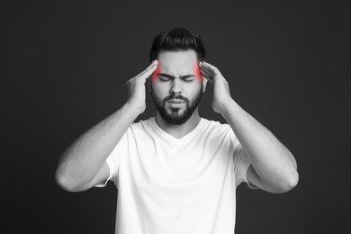 Young man suffering from headache on dark background. Black and white effect with red color accent