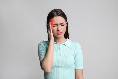 Young woman suffering from headache on grey background