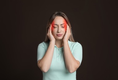 Young woman suffering from headache on dark brown background