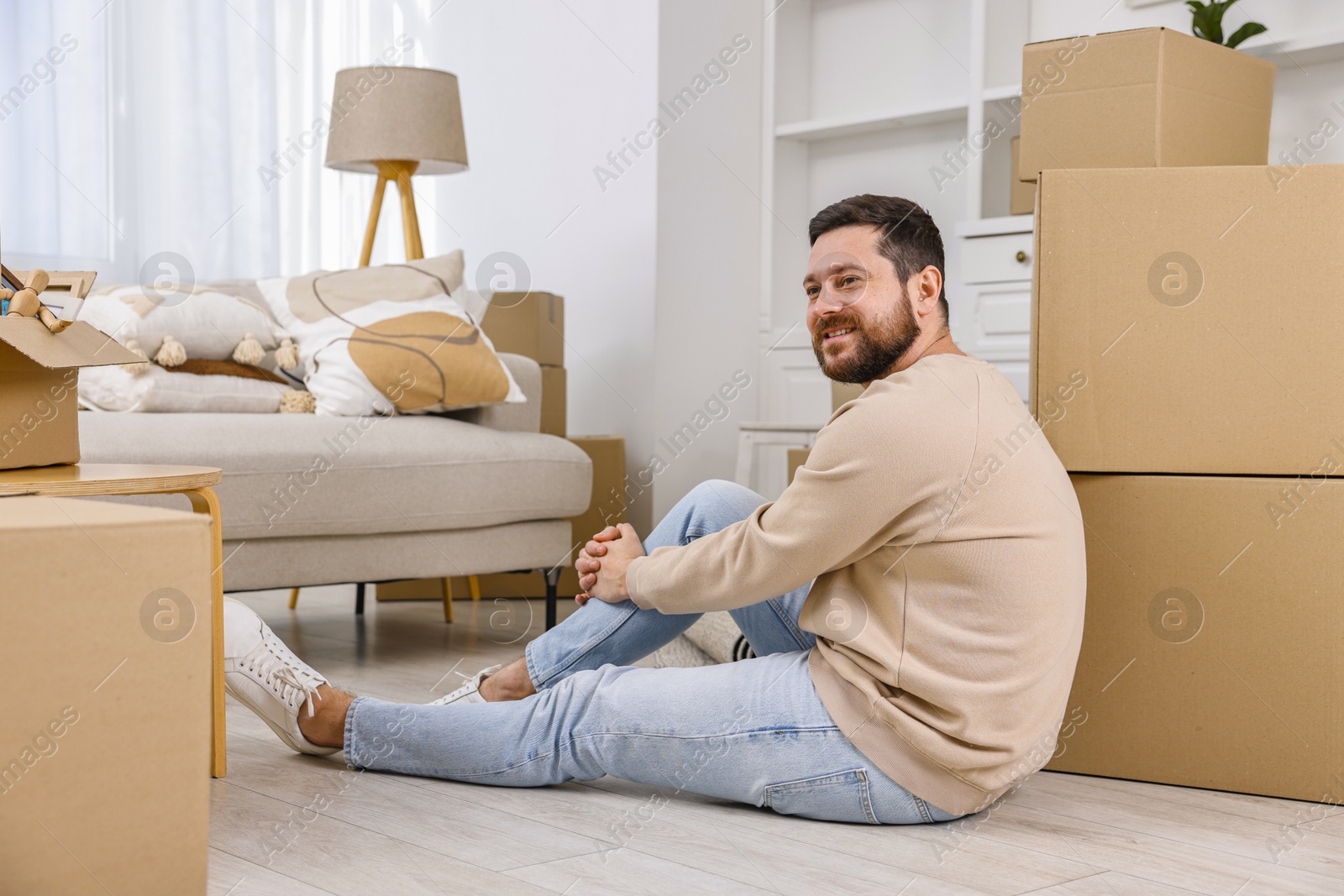 Photo of Moving day. Man resting on floor near cardboard boxes in his new home