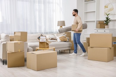 Photo of Moving day. Happy man with rug and cardboard box in his new home