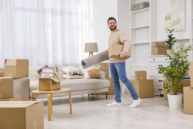 Photo of Moving day. Happy man with rug and cardboard box in his new home