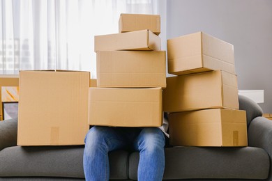 Photo of Moving day. Man with cardboard boxes on sofa in his new home