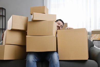 Photo of Moving day. Man with cardboard boxes on sofa in his new home