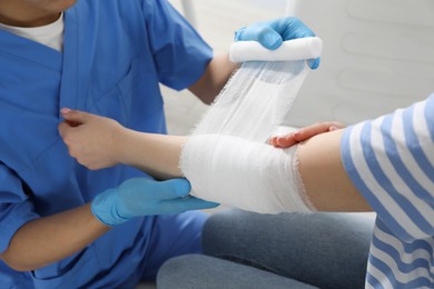 Doctor bandaging patient's elbow in clinic, closeup