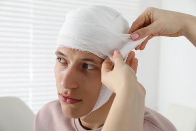 Doctor bandaging patient's head in clinic, closeup