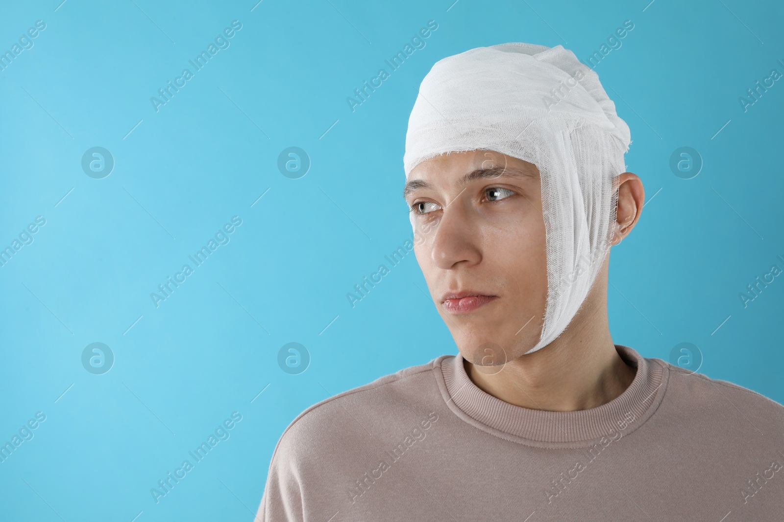 Photo of Man with head wrapped in medical bandage on light blue background, space for text