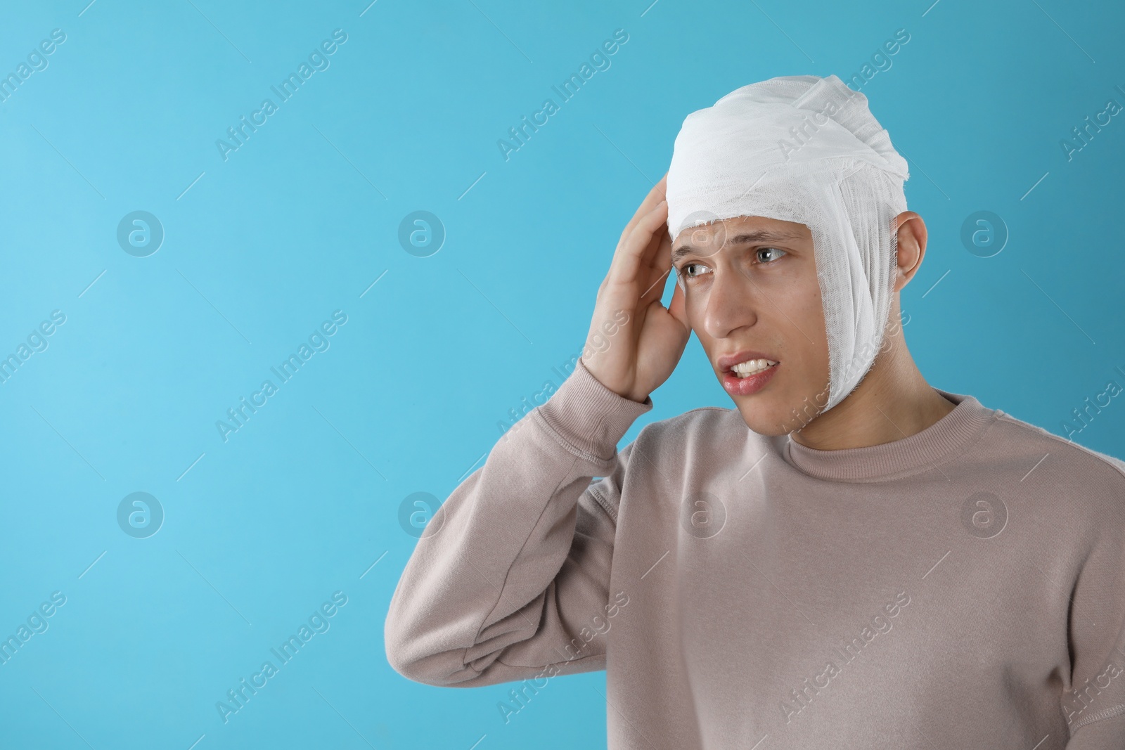 Photo of Man with head wrapped in medical bandage on light blue background, space for text