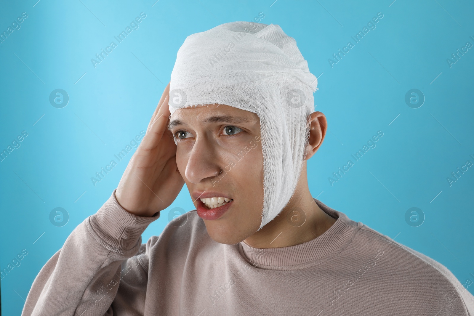 Photo of Man with head wrapped in medical bandage on light blue background