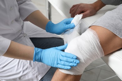 Photo of Doctor bandaging patient's knee in clinic, closeup