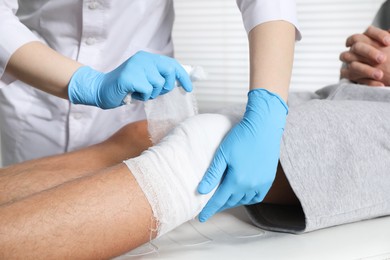 Photo of Doctor bandaging patient's knee in clinic, closeup