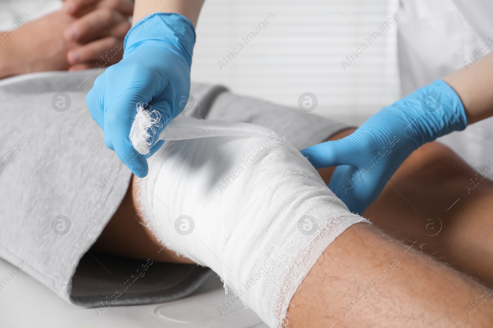 Photo of Doctor bandaging patient's knee in clinic, closeup