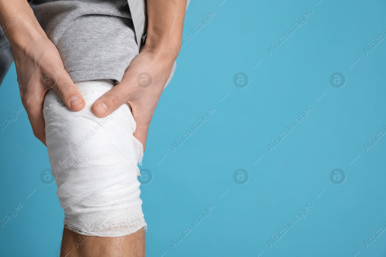 Photo of Man with medical bandage on his knee against light blue background, closeup. Space for text