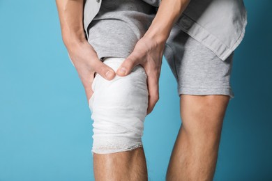 Photo of Man with medical bandage on his knee against light blue background, closeup