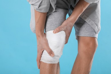 Photo of Man with medical bandage on his knee against light blue background, closeup