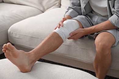 Photo of Man with medical bandage on his knee at home, closeup