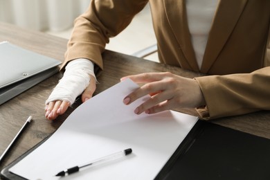 Photo of Woman with medical bandage on her wrist working at wooden table indoors, closeup