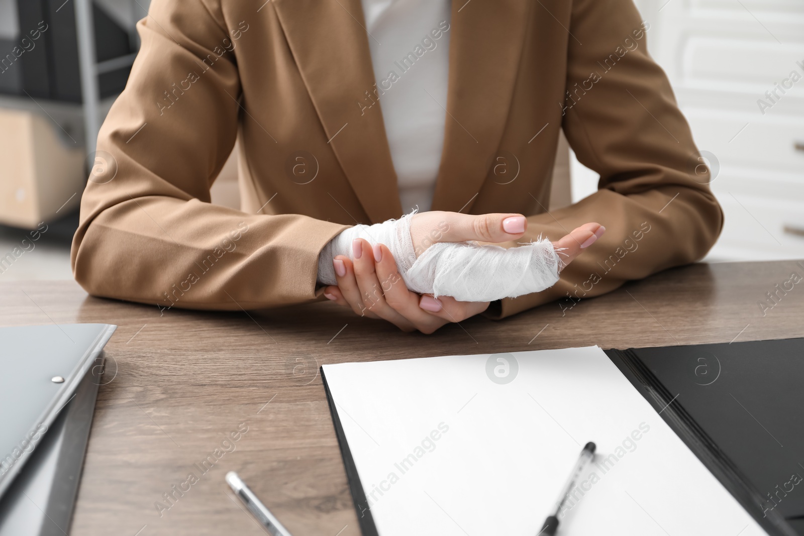 Photo of Woman with medical bandage on her wrist at wooden table indoors, closeup