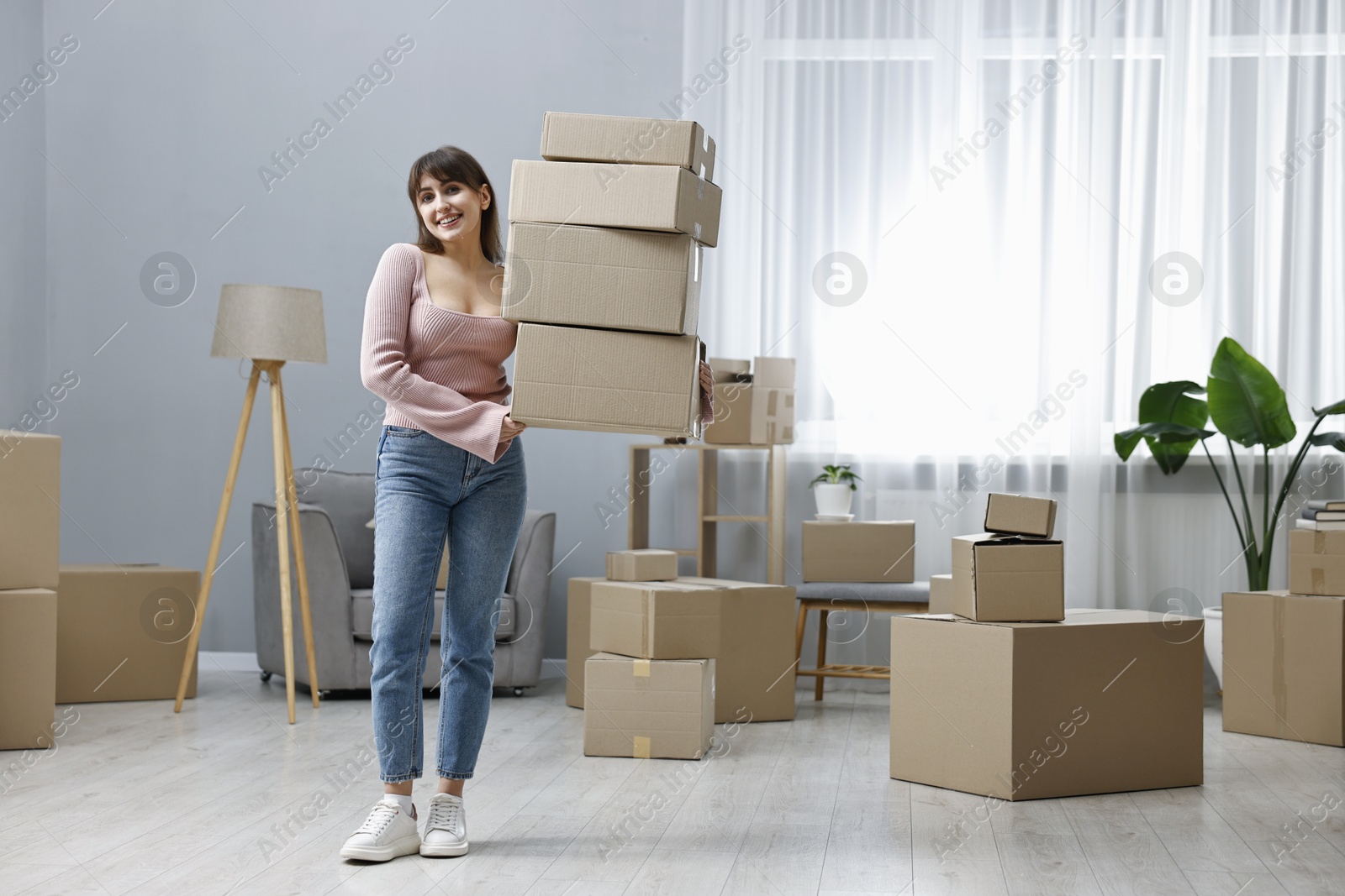 Photo of Moving day. Happy woman with cardboard boxes in her new home