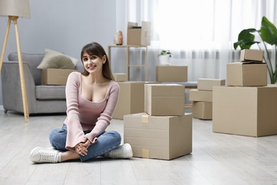 Photo of Moving day. Happy woman sitting on floor near cardboard boxes in her new home