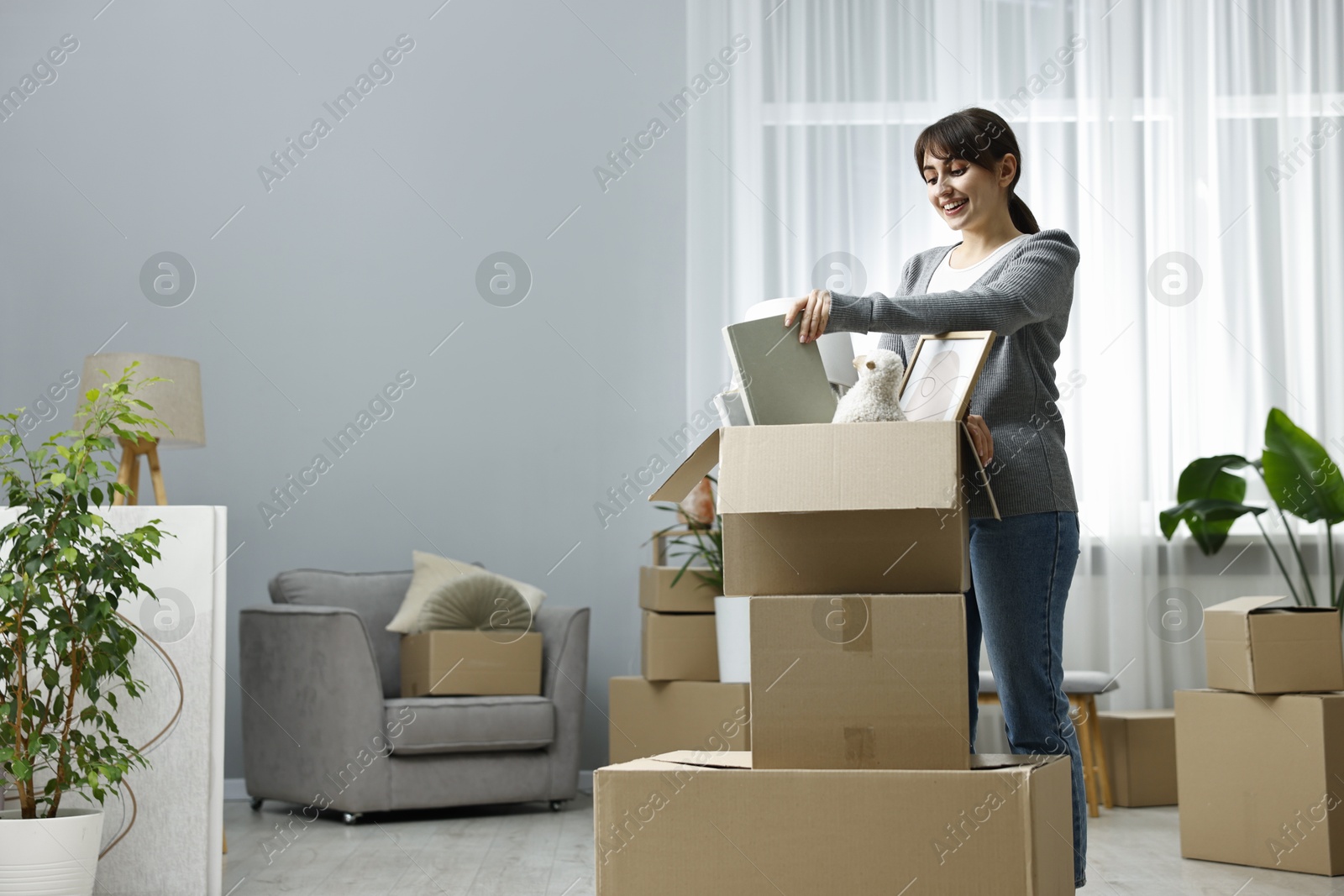 Photo of Moving day. Happy woman unpacking box in her new home