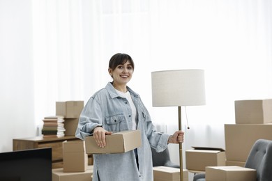 Photo of Moving day. Happy woman with lamp and cardboard box in her new home