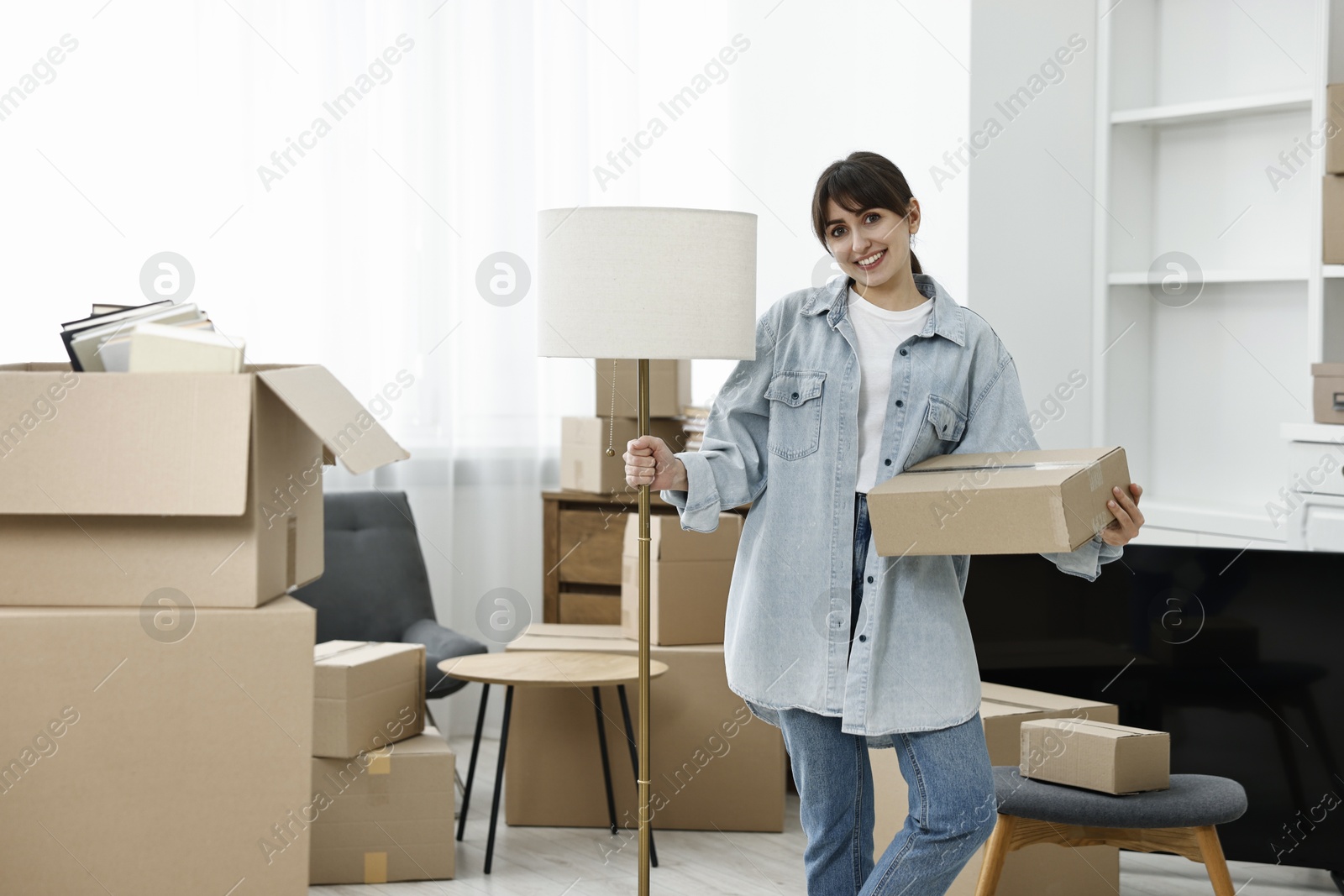 Photo of Moving day. Happy woman with lamp and cardboard box in her new home