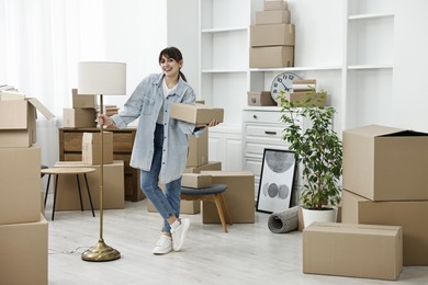 Moving day. Happy woman with lamp and cardboard box in her new home