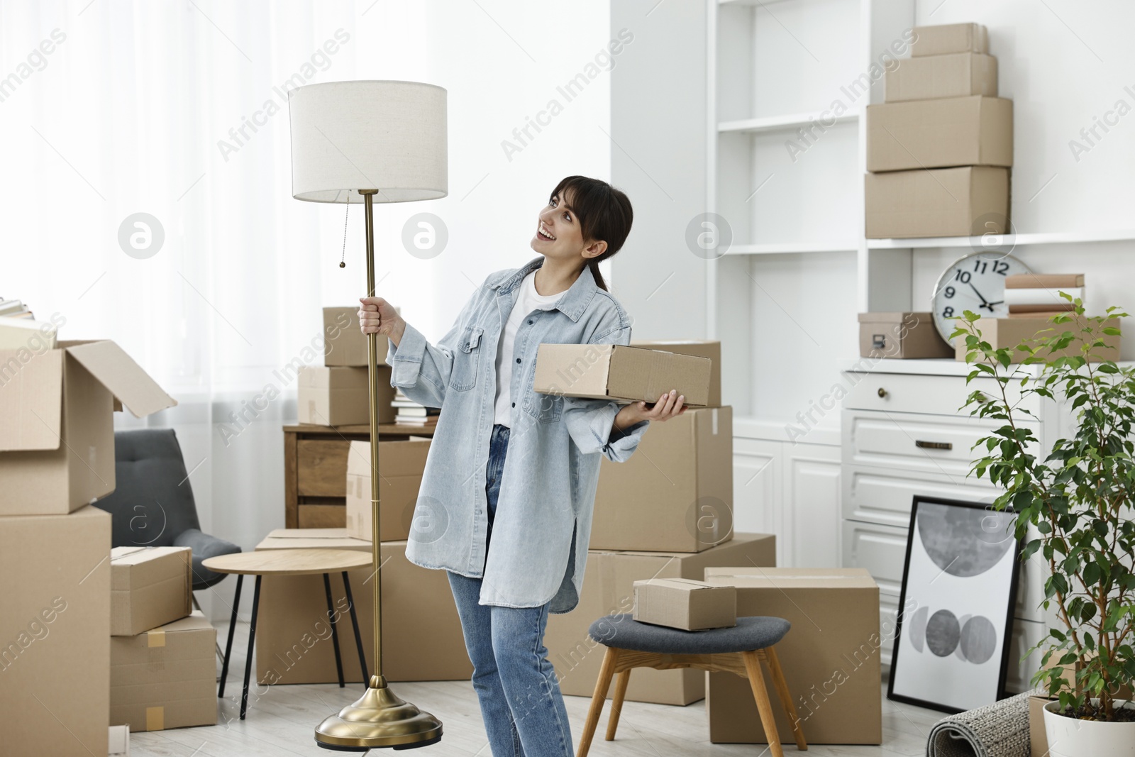 Photo of Moving day. Happy woman with lamp and cardboard box in her new home