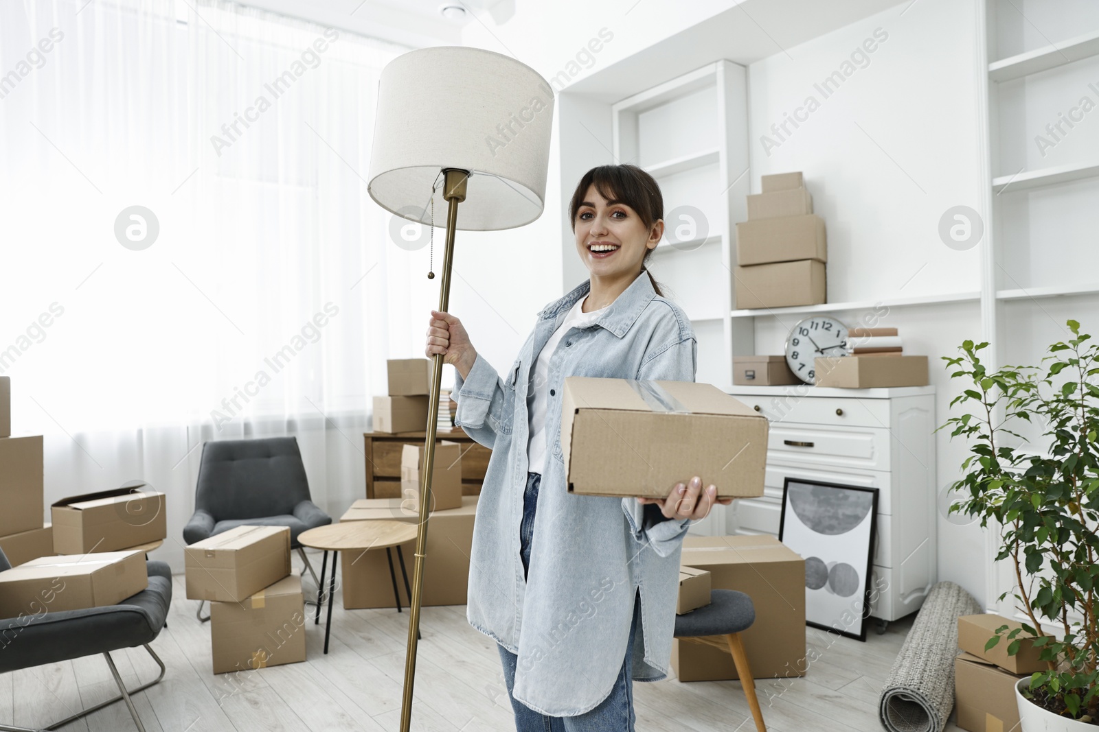 Photo of Moving day. Happy woman with lamp and cardboard box in her new home