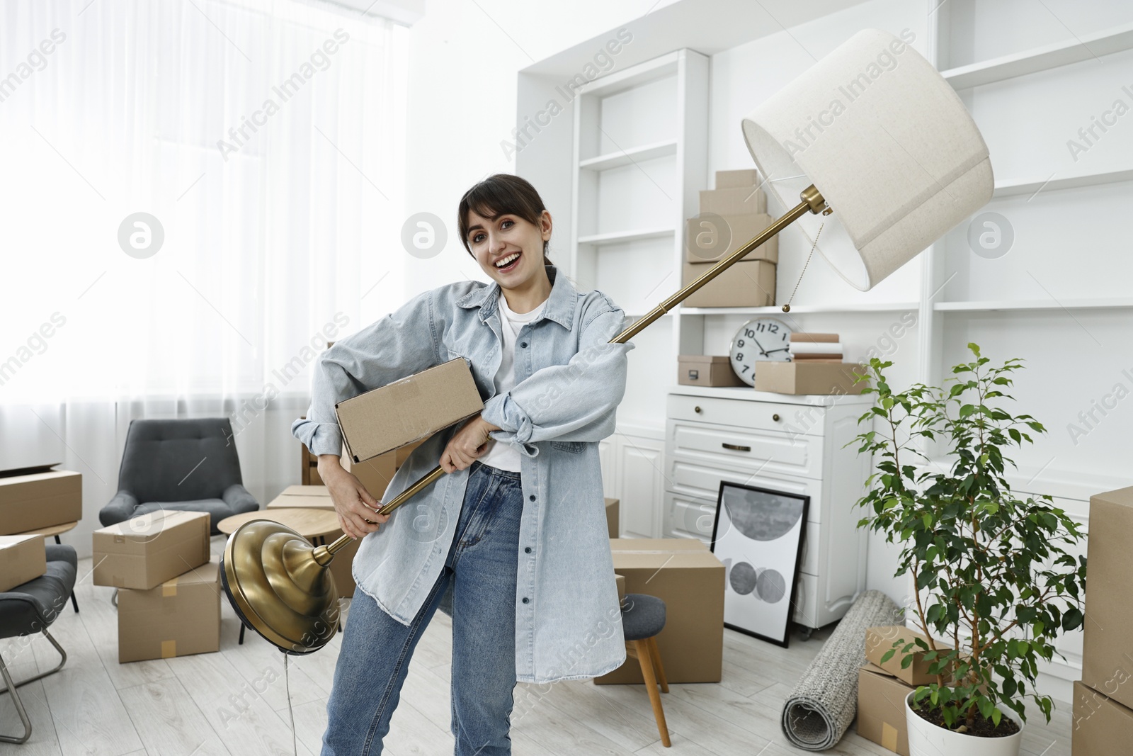 Photo of Moving day. Happy woman with lamp and cardboard box in her new home